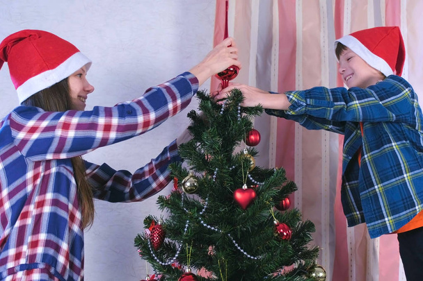 Mother and son in christmas hats set the spire on top of the Christmas tree. - Foto, Imagen