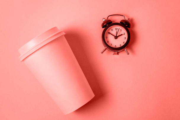 Απλά σχεδιασμό χαρτιού καφέ Κύπελλο και ξυπνητήρι χρωματιστό στο καθιερώνον τη μόδα χρώμα του φόντου των κοραλλιών που ζουν έτος 2019. Takeaway ποτό και πρωινό ρόφημα. Καλημέρα Ξυπνήστε ξύπνιοι έννοια. Χώρο αντίγραφο - Φωτογραφία, εικόνα