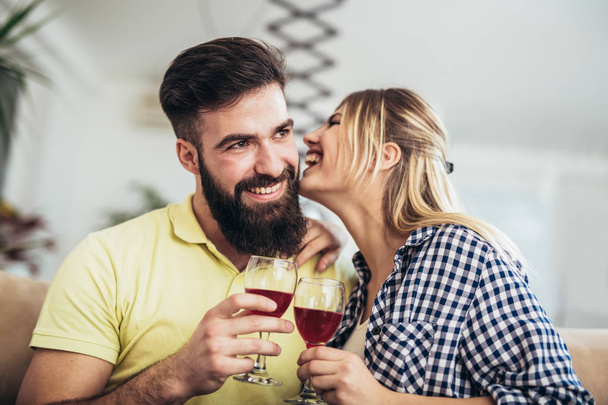 Photo of a young cheerful couple toasting at home with wine. - Фото, изображение