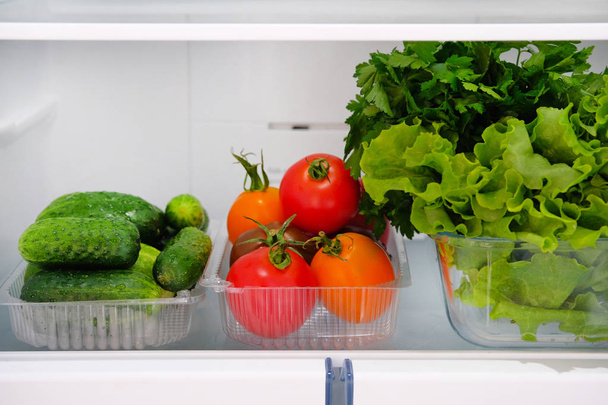 Open fridge. Healthy vegetarian food cucumbers, tomatoes, lettuce, parsley. Vegetables on shelf of refrigerator. Horizontal picture. - Foto, Bild