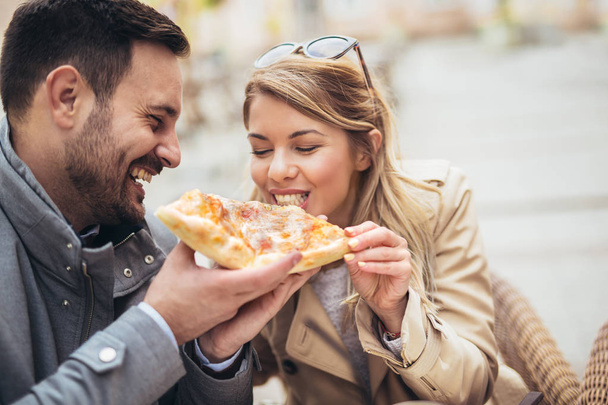 Kaunis rakastava pari istuu ulkona kahvilassa ja syö pizzaa
. - Valokuva, kuva