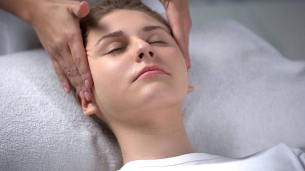 Beautician making relaxing facial massage, rubbing rejuvenating serum to woman - Foto, imagen