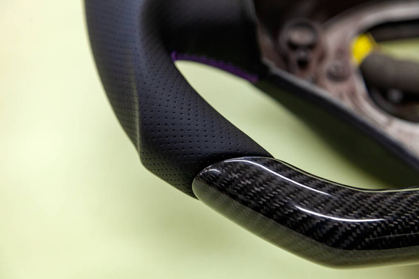 Close-up van een zwarte koolstofvezel stuurwiel kant met geperforeerd leer, gestikt met paarse wol op een auto onderdelen montage in een voertuigontwerp en tuning workshop. - Foto, afbeelding