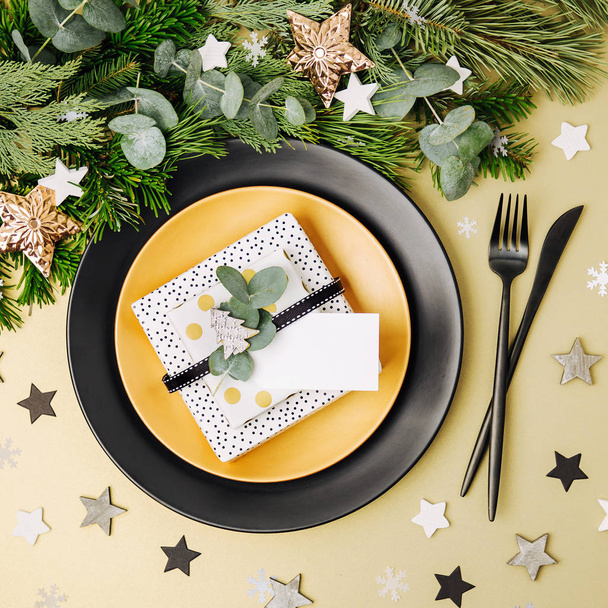 Festive table setting. Black Plates with gift and Christmas decorations with fir-tree branch. Flat lay, top view. - Zdjęcie, obraz