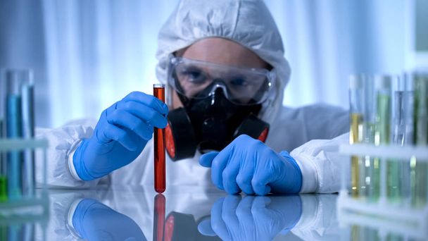 Scientist in gas mask holding test tube with dangerous substance, biohazard - Φωτογραφία, εικόνα