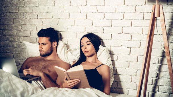 Couple Using Laptop Reading Book Before Sleeping - Фото, изображение