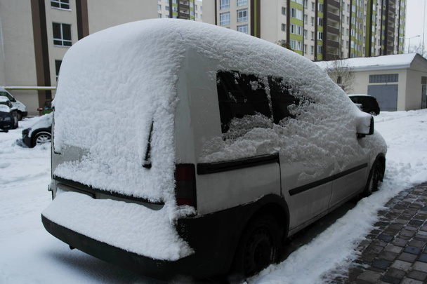 Mau tempo, carro branco coberto de neve no fundo de novas casas
 - Foto, Imagem