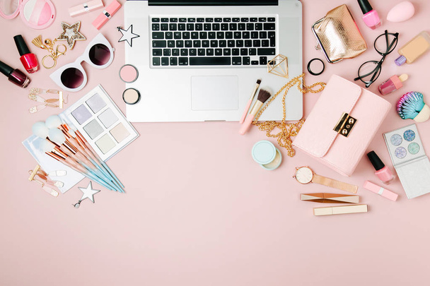 Fashion blogger workspace with laptop and female accessory, cosmetics products on pale pink table. flat lay, top view - Foto, Imagen