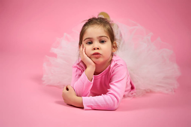 Portret van een schattig klein meisje in tulle rok op een roze achtergrond - Foto, afbeelding