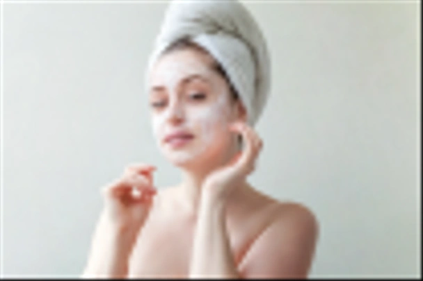 Portret van de schoonheid van een lachende brunette vrouw in een handdoek op de kop witte voedende masker of crème op gezicht op witte achtergrond geïsoleerd toe te passen. Huidverzorging reinigende spa relax concept - Foto, afbeelding