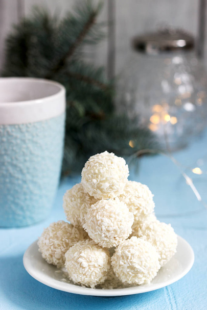 Coconut candies with white chocolate on a winter background with a garland, a candle and fir branches. Selective focus. - Photo, Image