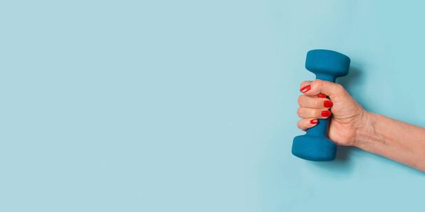 Female hand with blue dumbbell on blue pastel background. Sport concept. Healthy lifestyle. - 写真・画像