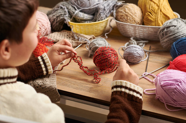 Criança está aprendendo a tricotar. Fios de lã coloridos estão na mesa de madeira. Eles são colocados como rosto sorridente. Fecho das mãos
. - Foto, Imagem