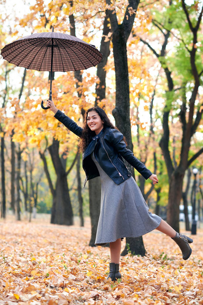 Frau mit Regenschirm posiert im Herbstpark. leuchtend gelbe Blätter und Bäume. imitiert sie den Wind. - Foto, Bild