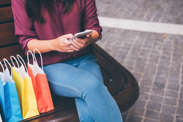 Consumerism, shopping, lifestyle concept, Young woman sitting near shopping bags and gift box while playing smartphone enjoying in shopping. - Fotoğraf, Görsel