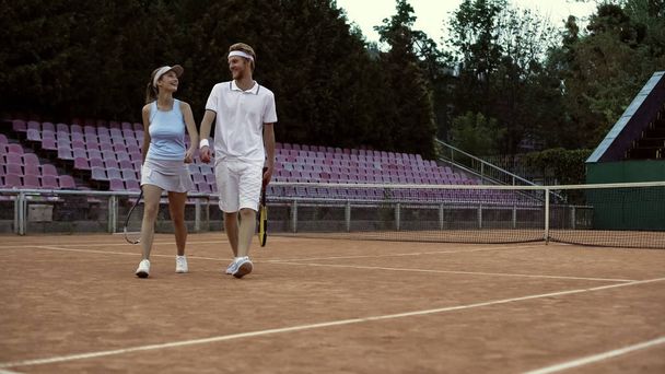 Smiling man and woman in white sportswear walking on court before tennis match - Zdjęcie, obraz