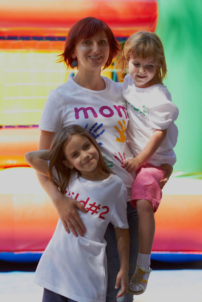 Young loving mother with her cute daughters sitting on the bouncing castle outdoors in a bright sunny day - Photo, Image