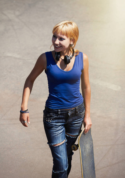 Punk skater chick in torn jeans ready to roll on her skateboard in a outdoor skatepark  - Fotó, kép