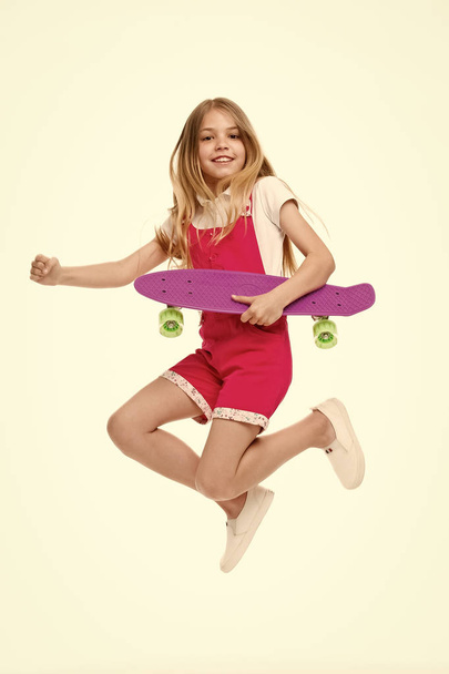 Find your freedom Small girl jump with skate board isolated on white. Child skater smile with longboard. Skateboard kid in pink jumpsuit. Sport activity and energy. Childhood and active games - Photo, image