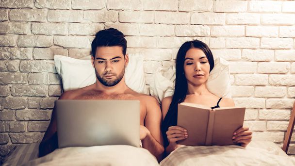 Couple Using Laptop Reading Book Before Sleeping - Foto, imagen