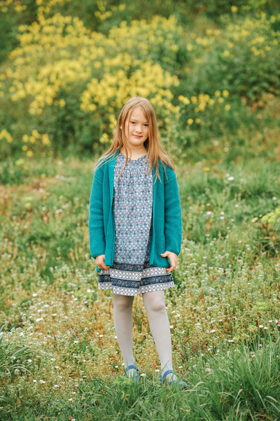 Outdoor spring portrait of cute 6-7 year old girl playing in yellow flowers field, wearing dress, green cardigan and grey tights - Fotó, kép