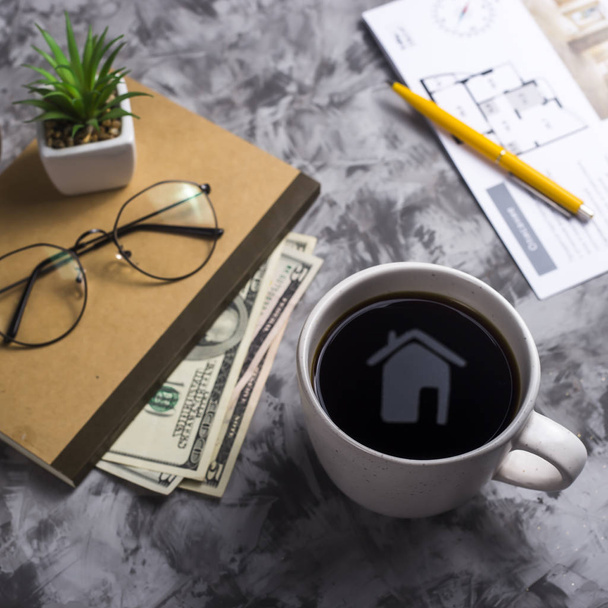 Reflection of the silhouette of a house with a cup of coffee - real estate purchase concept. Next to the notebook, glasses, money and an apartment plan - Foto, imagen