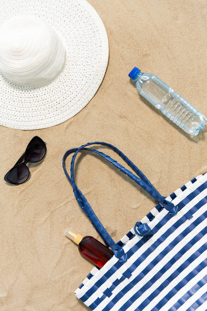 bolsa de playa, protector solar, gafas de sol y sombrero en la arena - Foto, Imagen