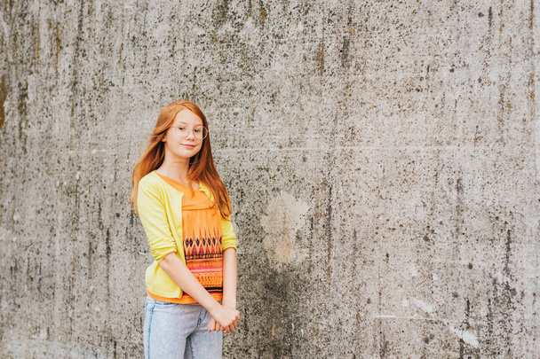 Outdoor portrait of pretty little girl with red hair, wearing orange t-shirt and yellow jacket - Photo, Image