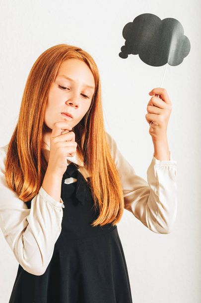 Studio shot of young red-haired kid girl holding paper thinking bubble, posing on white background - Photo, Image