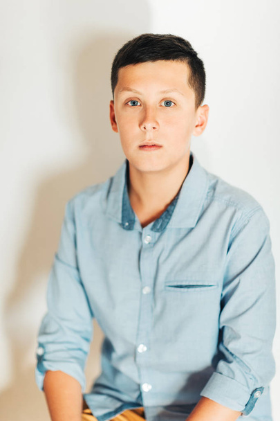 Portret van jonge tiener jongen die zich voordeed op een witte achtergrond, blauwe shirt dragen - Foto, afbeelding