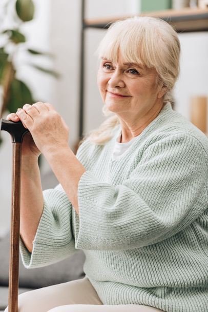 fröhliche Seniorin lächelt und hält Gehstock in der Hand  - Foto, Bild
