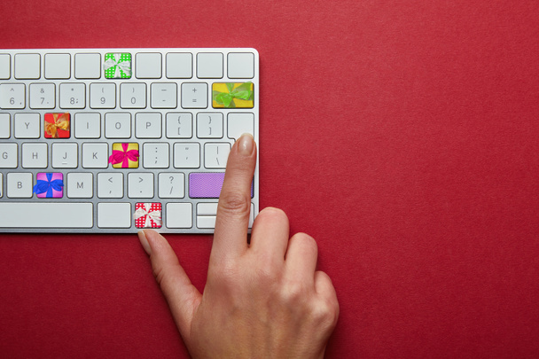 Cropped view of woman with computer keyboard with presents on buttons on red background, online christmas shopping concept - 写真・画像