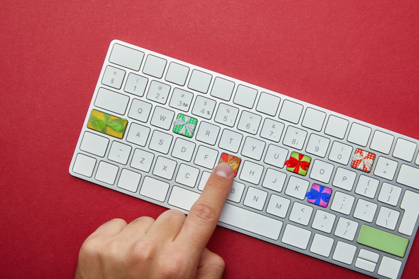 Cropped view of man pushing buttons with gifts on computer keyboard on red background, online christmas shopping concept - Foto, Imagem