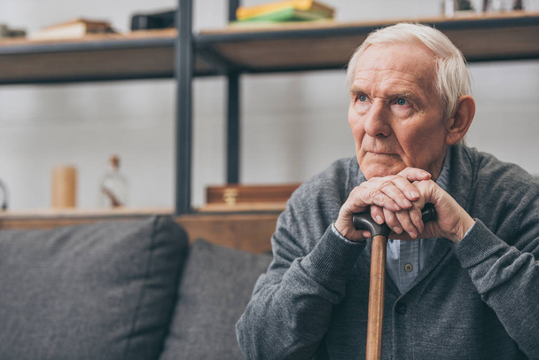 sad retired man with grey hair holding walking cane in living room  - Photo, Image
