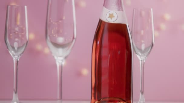 Roze mousserende wijn met dames hand en bril op roze achtergrond met kerstverlichting - Video