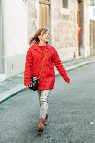 Outdoor fashion portrait of young girl walking down the street, wearing bright red stylish coat - Photo, Image