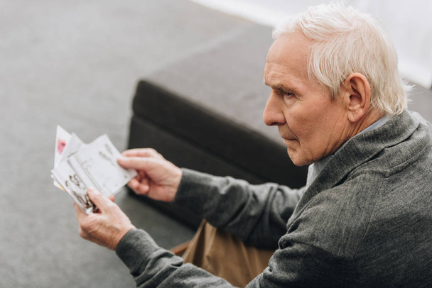 Trauriger Rentner mit grauen Haaren schaut sich zu Hause alte Fotos an - Foto, Bild