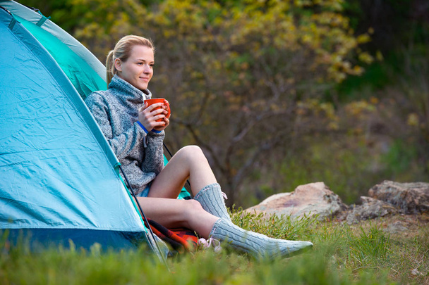 Traveler Girl com uma xícara de chá descansando perto de uma tenda contra o fundo verde da floresta
 - Foto, Imagem