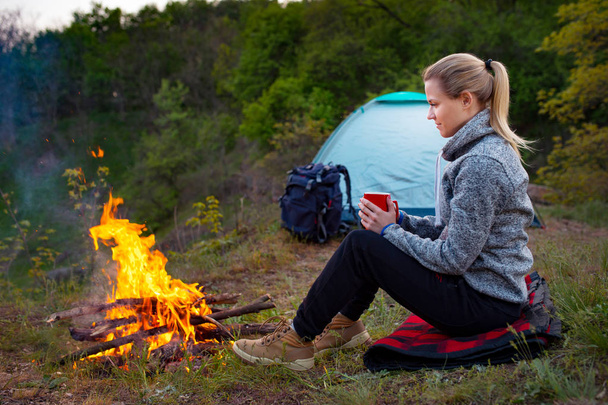 Nő utas pihen a tűz, a háttérben egy sátorban a gyalogút, a hegyekre és az erdő - Fotó, kép