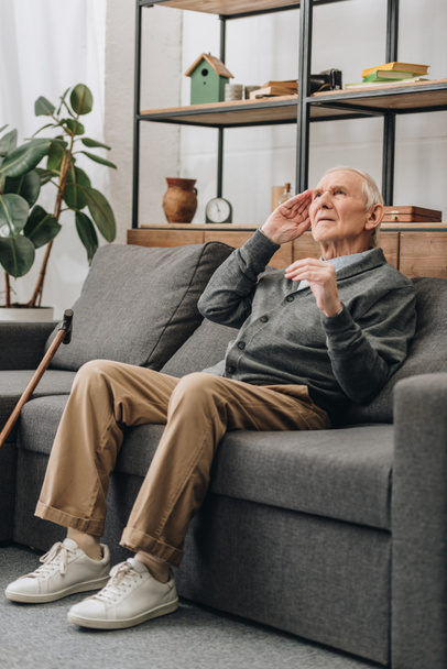 dreamy senior man with grey hair sitting on sofa in living room  - Foto, imagen