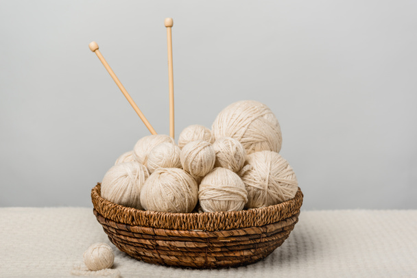 close up view of yarn clews and knitting needles in wicker basket on grey background - Foto, immagini