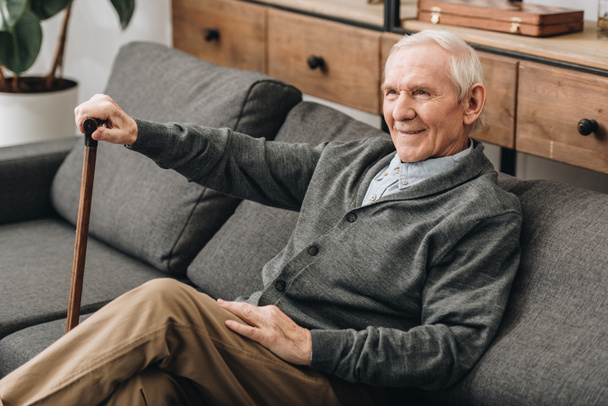 χαμογελώντας συνταξιούχος άνδρα που, καθισμένος στον καναπέ με περπάτημα από ζαχαροκάλαμο  - Φωτογραφία, εικόνα