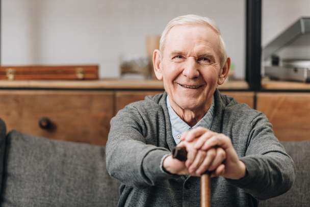 cheerful pensioner smiling and holding walking cane at home  - Photo, Image