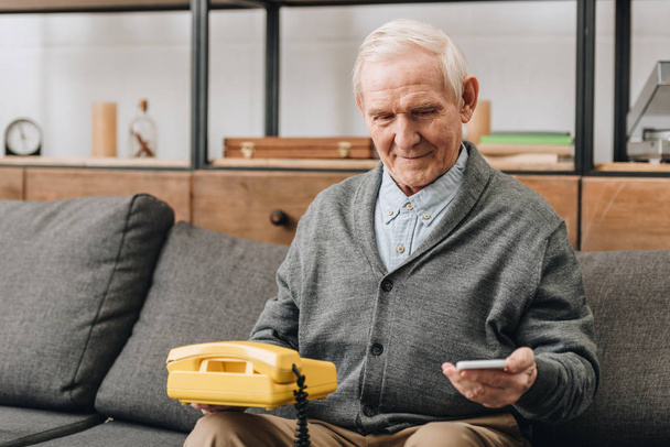 усміхнений чоловік на пенсії тримає смартфон і старий телефон вдома
 - Фото, зображення