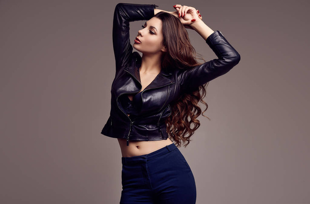 Portrait of young sexy girl with long hair in leather jacket on gray background in studio - Photo, Image