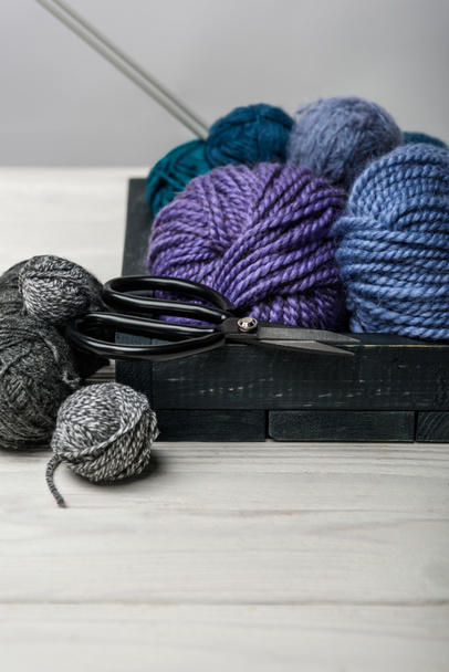 close up view of yarn balls and scissors in wooden box on white tabletop - Foto, afbeelding