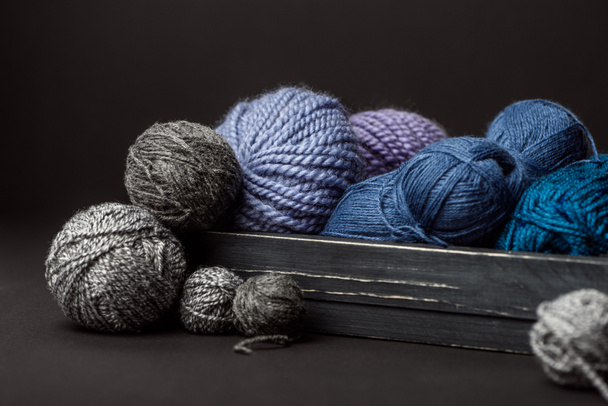 close up view of grey, purple and blue knitting clews in wooden box on black background - Fotoğraf, Görsel
