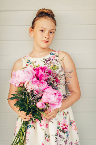 Portrait d'été d'adorable petite fille portant une belle robe occasionnelle, tenant un grand bouquet de pivoines
 - Photo, image