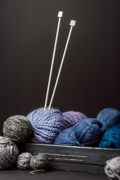 close up view of knitting clews and knitting needles in wooden box on black backdrop - Photo, Image
