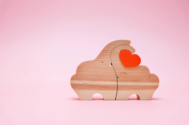 Beautiful wooden elephant figures holding the heart on pink background. Handmade products. The concept of Valentine's day. - Fotoğraf, Görsel